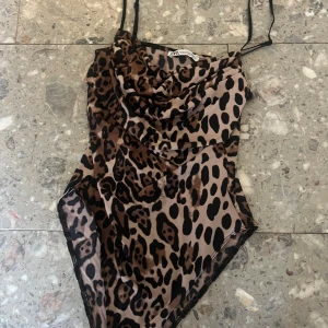Leopardmönstrad bodysuit från Zara - Snygg leopardmönstrad bodysuit från Zara med tunna axelband och draperad framsida. Perfekt för en djärv look! Passar s och m