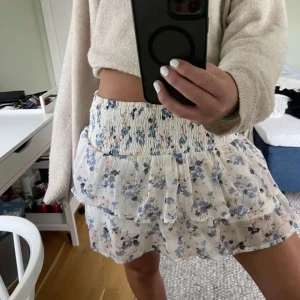 Blommig kortkjol med volang - Söt kortkjol med blommigt mönster i blått och vitt. Kjolen är i väldigt bra skick, storlek m men passar även mindre och större storlekar.💞 Lånade bilder!! Skriv för fler bilder eller frågor! 