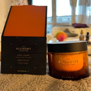 Body Cream från The Alchemy Collection - Lyxig body cream från The Alchemy Collection av Rituals, med doft av amber och myrra. Kommer i en elegant brun glasburk med svart lock och förpackad i en stilren svart kartong med orange insida. Perfekt för att återfukta och vårda huden.