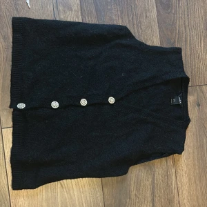 Svart kofta med glittriga knappar - Elegant svart kofta med glittriga knappar som ger en lyxig touch. Perfekt för att klä upp en enkel outfit. Koftan har en klassisk design med ribbade kanter. Perfekt för olika event du vill klä upp dig på.  Knappt använd😊❤️