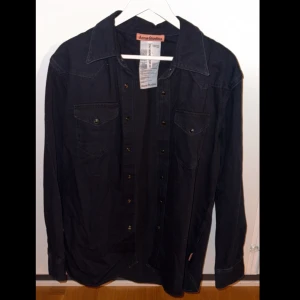 Svart jeans skjorta från Acne Studios - Snygg svart jeans skjorta från Acne Studios med långa ärmar och klassisk krage. Skjortan har knappar framtill och två bröstfickor med knappstängning. Har använts nångång för att testa så är som helt ny. 