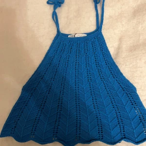 Blå stickad topp från Zara - Snygg blå stickad topp från Zara med tunna axelband och ett fint hålmönster. Perfekt för varma sommardagar. Toppen har en lätt utsvängd form och knytband vid axlarna.