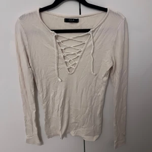 Beige ribbad tröja från Vila - Säljer en stilren beige ribbad tröja från Vila med snörning framtill. Tröjan har långa ärmar och en v-ringad design som ger en trendig look. Perfekt för både vardag och speciella tillfällen.