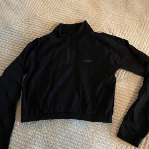 Svart långärmad tröja från ICANIWILL - Snygg svart långärmad tröja från ICANIWILL med halv dragkedja framtill. Perfekt för träning eller en avslappnad dag. Enkel och stilren design med diskret logga på bröstet.