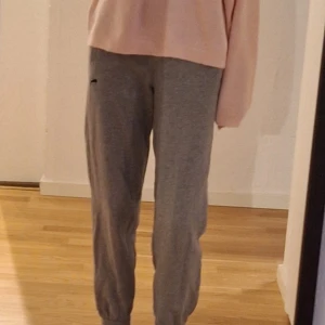 Grå mjukisbyxor med tryck - Säljer ett par grå mjukisbyxor med svart pumatryck på sidan. Byxorna har en avslappnad passform och resår vid anklarna för extra komfort. Perfekta för en chill dag hemma eller en snabb tur till affären. Är I storlek 152 men ja ha XS och ja kan ha dem