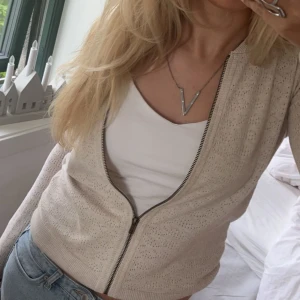 Beige kofta med dragkedja - Snygg beige kofta med dragkedja framtill. Koftan har ett diskret hålmönster och ribbade kanter vid ärmslut och nederkant. Perfekt för lager-på-lager-stil. Inga difekter, bra skick!