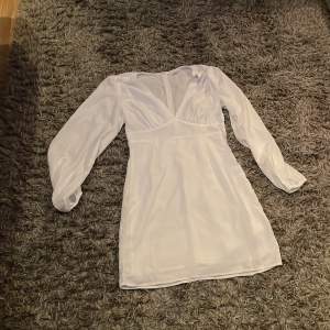 Elegant vit klänning med v-ringning och långa ärmar från Nelly x Glamorous. Perfekt för en stilren look med sin korta längd och figurnära passform. Klänningen har en dragkedja i sidan för enkel påklädning. Använd en gång