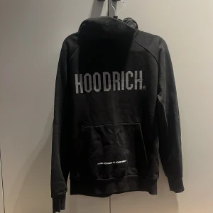 Svart hoodie från Hoodrich - Säljer en svart hoodie från Hoodrich med stor logga på framsidan. Tröjan har långa ärmar och en praktisk ficka framtill. Perfekt för en avslappnad stil.