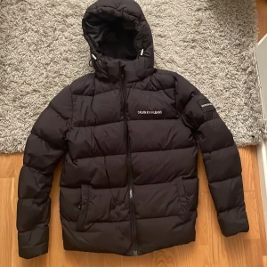 Calvin Klein Dunjacka - Säljer en svart dunjacka från Calvin Klain Jeans som är i storlek M. Den är i väldigt bra skick förutom från ett väldigt litet jack ovanför märket på bröstet. Köpte för 1500 