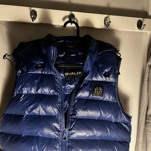 BVALDI VÄST - Pris kan diskuteras! Snygg blå dunväst med dragkedja och huva. Perfekt för kyliga dagar och ger en sportig look. Västen har en quiltad design och en liten logotyp på bröstet. Pefekt för både Grisch o street style då du kan matcha med den väldigt unikt går för 1899kr mitt pris 799kr