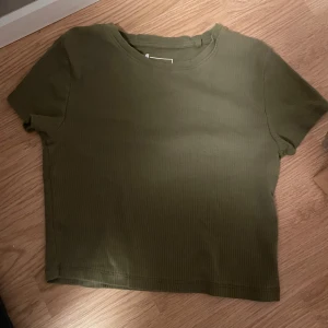 Olivgrön ribbad topp från FSBN Sister - Säljer en olivgrön ribbad topp från FSBN Sister. Den har en croppad passform och korta ärmar.