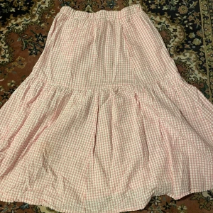 Rutig kjol från Monki - Söt rosa och vit rutig kjol från Monki i storlek S. Kjolen har en volangdetalj och är perfekt för sommaren! Tillverkad i ett lätt och bekvämt material.