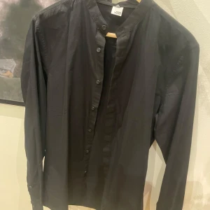 Svart skjorta från Visual clothing project - Snygg svart skjorta  med en stilren design. Skjortan har långa ärmar och knappar framtill. Perfekt för en minimalistisk look.