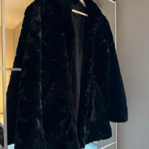 Svart pälsjacka - Snygg svart pälsjacka med långa ärmar och knäppning framtill. Perfekt för att hålla sig varm och stilren under kyliga dagar.