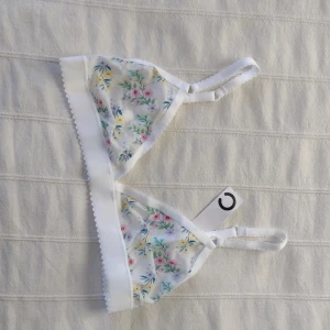 Blommig vit bralette/topp/bh - Söt blommig bralette i vitt med justerbara axelband och hakknäppning bak. Oanvänd. Storlek S. Kan skickas med ett frimärke (22 kr).