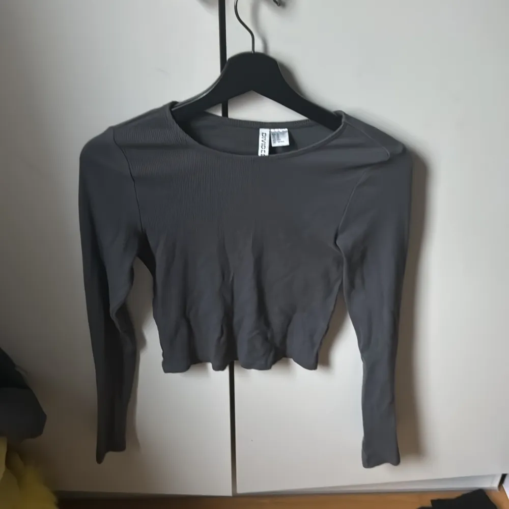 Säljer en stilren grå ribbad topp från Divided. Den har en croppad passform och långa ärmar, perfekt för en trendig look. Toppen är i storlek XS och passar utmärkt till både jeans och kjol. Från hm!. Neuletakit & Villapaidat.
