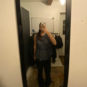 Blå prickig blus - Säljer en blå blus med vita prickar. Blusen har ärmlös design och en volangdetalj som ger en fin siluett. Perfekt för både vardag och speciella tillfällen.