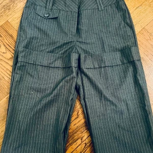 Grå randiga kostymbyxor - Snygga grå lågmidjade kostymbyxor med diskret randigt mönster. Byxorna har knappar både fram och bak.