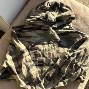 Camouflage hoodie från H&M Divided - Säljer en cool camouflage hoodie från H&M Divided. Perfekt för en avslappnad stil med sin klassiska huva och mjuka material. Passar utmärkt för höst och vår. Croppad