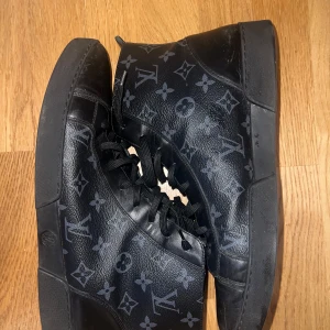 Svarta sneakers från Louis Vuitton - Snygga svarta sneakers i skinn från Louis Vuitton med det ikoniska monogrammönstret. Skorna har snörning och en diskret logotyp på sulan. Perfekta för en stilren look.