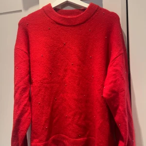 Röd tröja med pärlor från H&M - Snygg röd tröja från H&M dekorerad med små pärlor. Den har en rund halsringning och långa ärmar, perfekt för att ge lite extra stil till din outfit. Tröjan är i en härlig röd färg som verkligen poppar.