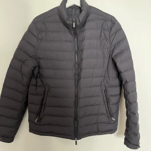 Grå dunjacka från Massimo Dutti - Säljer en snygg och stilren grå dunjacka från Massimo Dutti. Jackan har en quiltad design med dragkedja framtill och två praktiska fickor med dragkedjor. Den är både vattenavvisande och vindtät, perfekt för kyliga dagar. Insidan har en mjuk och bekväm känsla. Passar perfekt för höst och vinter!