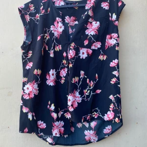 Blommig ärmlös topp från Soul River - Säljer en superfin ärmlös topp från Soul River i storlek M. Den har ett vackert blommigt mönster i rosa och vitt på en svart bakgrund. Perfekt för sommardagar eller en avslappnad fest. Toppen är i ett lätt och bekvämt material.