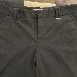 Blåa kostymbyxor från Calvin Klein - Säljer ett par stilrena blå kostymbyxor från Calvin Klein. De är i ett klassiskt snitt med hällor för bälte och en snygg knappdetalj på bakfickan. Perfekta för både kontoret och finare tillfällen. Bra skick, storlek 0, motsvarar 34