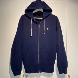 Polo Ralph Lauren Zip-Hoodie Navy - Ralph Lauren Fleece Zip-Hoodie i marinblå färg med gul häst. Använd en hel del men i dugligt skick. Modellen Produceras ej längre. Storlek M. Passar perfekt att både dressa upp och ner. Nypris 1900kr. Kvalitativ & bekväm. Pris kan diskuteras. Hörs i DM! 