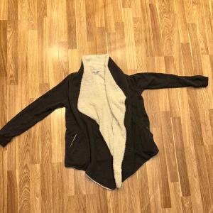 Mysig brun fleecejacka - En supermysig grå fleecekofta med vit fluffig insida. Perfekt för kyliga höst- och vinterdagar. Koftan har en öppen design utan knappar eller dragkedja, vilket gör den lätt att slänga på sig. Från New Yorker storlek S. Oanvänd!! 