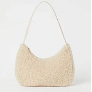 Beige axelväska i teddy-material - Superfin beige axelväska i mysigt teddy-material. Den har en praktisk dragkedja upptill och en design som passar perfekt till höst- och vinteroutfits. Väskan är både trendig och funktionell, perfekt för att bära dina dagliga essentials. Nypris 199kr