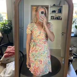 Blommig sommarklänning - Säljer en superfin blommig sommarklänning med korta ärmar och omlott-design. Klänningen har en v-ringad hals och ett knytband i midjan som ger en smickrande passform. 