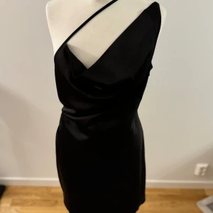 Svart oneshoulder klänning från Chloé B - Säljer en elegant svart oneshoulder klänning från Chloé B. Den har en stilren design med en dragkedja i ryggen för enkel påklädning. Perfekt för festliga tillfällen!