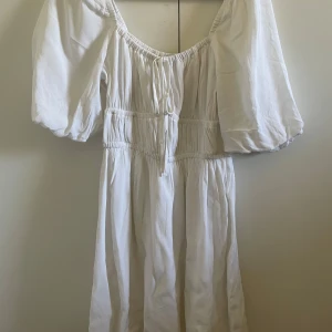 Vit klänning från BikBok - Säljer en superfin vit klänning från BikBok i storlek XS. Den har en offshoulder-design med puffiga ärmar och en smockad midja som ger en snygg passform. Perfekt för sommaren eller vid finare tillfällen! Endast använd en gång, köpt för 399kr😊
