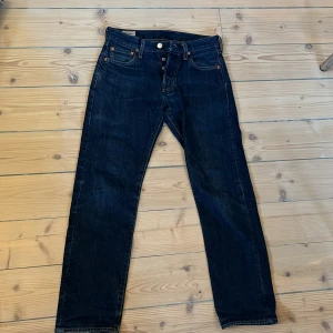 Mörkblåa Levis 501 jeans - Jeansen är i bra skick då jag inte använt de så mycket, det är bara lite slitningar längst ner på byxan. Storleken är W27 L30 och sitter som slim fit jeans
