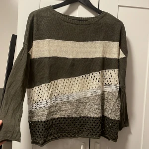 Randig stickad tröja i jordnära toner - Säljer en superfin stickad tröja med randigt mönster i jordnära färger som olivgrön, beige och grå. Tröjan har långa ärmar och ett luftigt, hålmönstrat parti som ger en cool look. Perfekt för höst och vår när du vill vara både stilren och bekväm. Passar perfekt till jeans eller kjol!