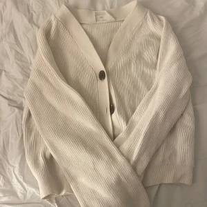 Vit ribbad kofta från H&M - Säljer en superfin vit ribbad kofta från H&M. Den har stora knappar framtill och är perfekt för både vår och höst. Koftan är i mycket bra skick och passar perfekt för en stilren look. Perfekt att ha över en t-shirt eller blus!