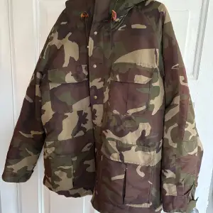 Säljer en cool camouflagejacka från These Glory Days i storlek medium. Jackan har ett klassiskt camouflagemönster och är fodrad med ett rött och blått rutigt tyg. Perfekt för höst och vår, med praktiska fickor och en skön huva. Passar både för vardag och äventyr!