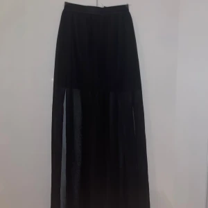 Svart långkjol i transparent material - Säljer en svart långkjol i ett snyggt transparent material. Perfekt för en kväll ute eller en festlig tillställning. Kjolen har en elastisk midja för bekväm passform och ger en elegant look med sin långa längd. 