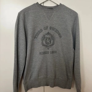 Grå sweatshirt från Tiger of Sweden - Säljer en grå sweatshirt från Tiger of Sweden i storlek S. Tröjan har ett tryck med texten 'Tiger of Sweden Since 1903' på framsidan. Knappt använd, mycket bra skick