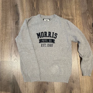 Grå tröja från Morris - Säljer en snygg grå tröja från Morris med texten 'PHYS. ED. EST. 1968' i svart på bröstet. Tröjan är i bra skick och har långa ärmar med ribbade muddar. Perfekt för en avslappnad stil eller för att hålla sig varm under kyligare dagar.