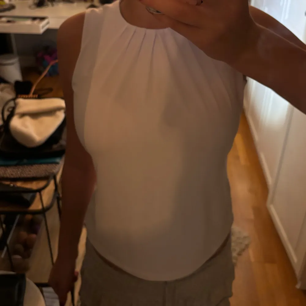 Säljer en stilren vit ärmlös topp från Calvin Klein i mycket bra skick. Toppen har en elegant rynkad detalj vid halsen och är perfekt för både vardag och fest. Materialet känns mjukt och bekvämt mot huden. Passar perfekt till sommarens alla tillfällen!. Toppar.