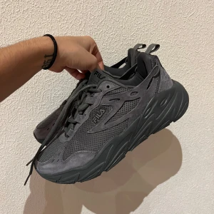 Grå sneakers från Fila | OANVÄNDA - Säljer ett par grå Fila sneakers i mycket bra skick. De har en chunky sula och är gjorda i syntetmaterial med meshdetaljer för extra andningsförmåga. Perfekta för både vardag och träning. Skorna har snörning och en stilren design som passar till det mesta. Passar 38-39