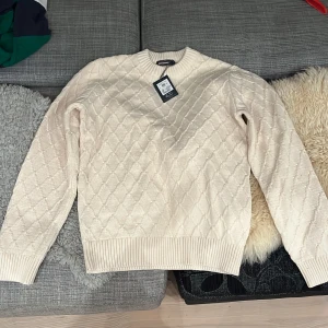 Beige stickad tröja från Dressmann - Säljer en snygg beige stickad tröja från Dressmann i storlek M. Tröjan har ett diskret rutmönster och är perfekt för kyliga dagar. Den är långärmad med ribbade muddar och nederkant. Passar både till vardags och lite finare tillfällen. Helt ny med tag kvar! Super skönt med. Nypris  599 kr. 