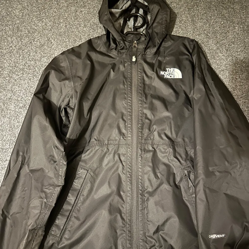 Säljer en svart regnjacka från The North Face i mycket bra skick. Jackan har en praktisk huva och dragkedja framtill. Perfekt för regniga dagar och outdoor-äventyr. Den är lätt och smidig att bära med sig. Passar både till vardags och friluftsliv.. Takit.