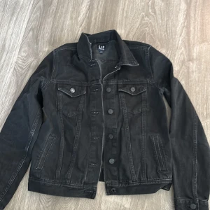 Svart jeansjacka från GAP - Säljer en klassisk svart jeansjacka från GAP i bra skick. Den har en normal passform med långa ärmar och knappar framtill. Perfekt för vår och höst, och funkar till nästan alla outfits. 🖤
