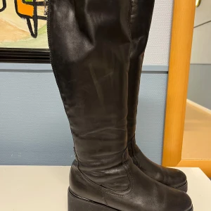 Svarta stövlar från Remonte - Snygga svarta stövlar från Remonte i skinn med dragkedja baktill. Perfekta för höst och vinter med en stilren design och bekväm passform. De har en diskret klack och är i mycket bra skick. Fodrade på insidan i äkta ull.