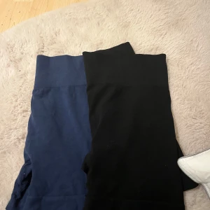 Svarta och blåa träningstights - Säljer två par träningstights i svart och blått. De är högmidjade med en bred ribbad midja för extra komfort. Perfekta för gymmet eller yoga! Materialet är stretchigt och andas bra.