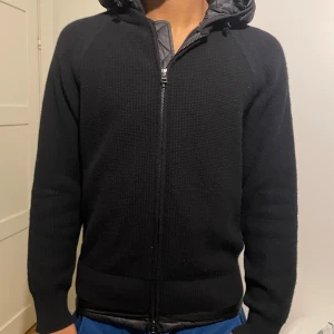 Svart jacka från Moncler - Säljer en snygg svart jacka från Moncler i mycket bra skick. Den har en dragkedja framtill och en quiltad huva. Perfekt för höst och vinter med sin stilrena design och varma material. Jackan har långa ärmar och Moncler-loggan på ärmen. Passar både till vardags och lite finare tillfällen.