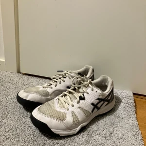 Vita och svarta Asics, inneskor. - Säljer ett par vita och svarta Asics sneakers i bra skick. Storlek EU 41.5. Sköna och stabila med bra grepp.